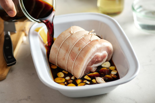 Tied pork poured with soy sauce in bowl with cut garlic.