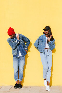 Funny cool couple wearing denim clothes in yellow wall. 