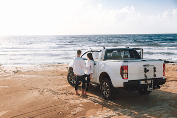 Fototapeta na wymiar A young couple with a pick up truck on a deserted beach.young couple by pick-up truck parked on beach