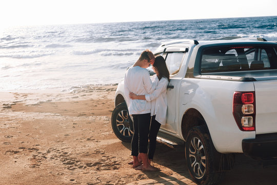 A young couple with a pick up truck on a deserted beach.young couple by pick-up truck parked on beach