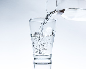 Pouring water into glass from a jar isolated on white background