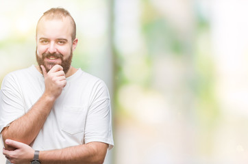 Young caucasian hipster man wearing casual t-shirt over isolated background looking confident at the camera with smile with crossed arms and hand raised on chin. Thinking positive.
