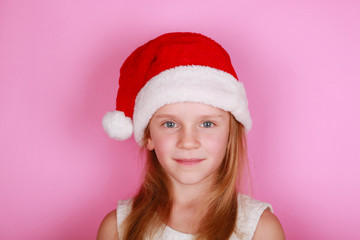 Happy smiling girl in Santa cap and white dress on a pink background, copy space. 
