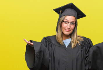 Young beautiful woman wearing graduated uniform over isolated background clueless and confused expression with arms and hands raised. Doubt concept.