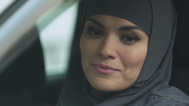 Muslim woman rolling car window down to check road, attentive driver, closeup