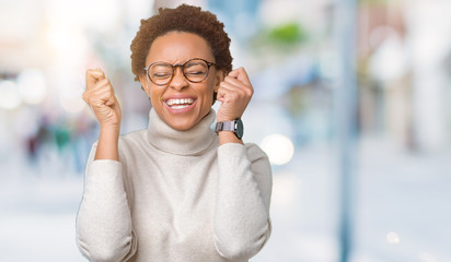 Young beautiful african american woman wearing glasses over isolated background excited for success with arms raised celebrating victory smiling. Winner concept.