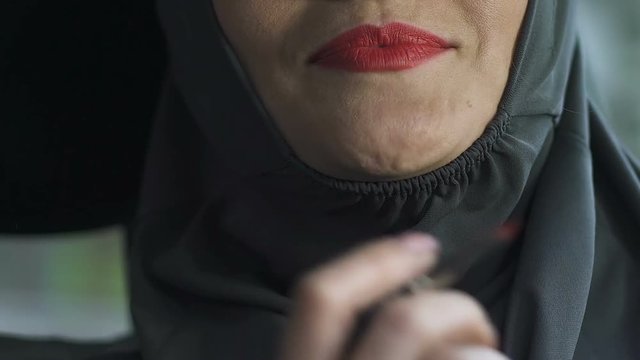 Woman in hijab applying red lipstick, ban on bright makeup in public places