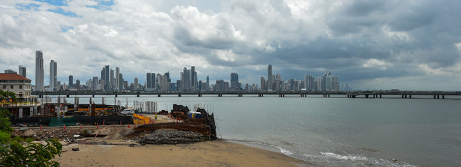 Hot day in Panama city as a rainstorm brews quickly over city skyline.  Tall buildings shimmer in heatwaves rising in humid air. Construction workers laboring in old section of the city in foreground.