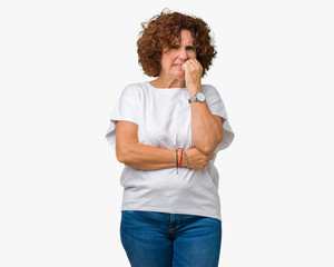 Fototapeta na wymiar Beautiful middle ager senior woman wearing white t-shirt over isolated background looking stressed and nervous with hands on mouth biting nails. Anxiety problem.