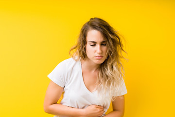 Young beautiful blonde woman over yellow background with hand on stomach because nausea, painful disease feeling unwell. Ache concept.