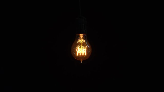 Power saving concept. Tungsten light bulb turns on and off on dark background. Shot in 4k resolution