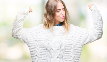 Beautiful young blonde woman wearing winter sweater over isolated background showing arms muscles smiling proud. Fitness concept.
