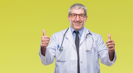 Handsome senior doctor man over isolated background success sign doing positive gesture with hand, thumbs up smiling and happy. Looking at the camera with cheerful expression, winner gesture.