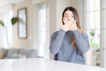 Fototapeta na wymiar Young beautiful woman wearing winter sweater at home shocked covering mouth with hands for mistake. Secret concept.