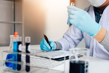 Scientist recording making note on book with his findings test tube in lab.