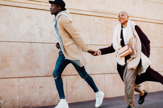 Cool multiethnic couple holding hands running on the street. 