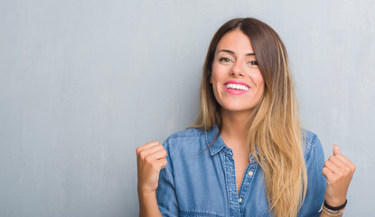 Young adult woman over grunge grey wall wearing denim outfit celebrating surprised and amazed for success with arms raised and open eyes. Winner concept.