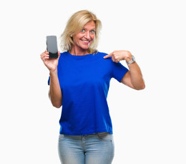 Middle age blonde woman showing blank screen of smartphone over isolated background with surprise face pointing finger to himself