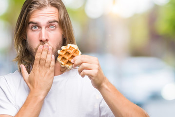 Young handsome man with long hair over isolated background eating waffle cover mouth with hand...