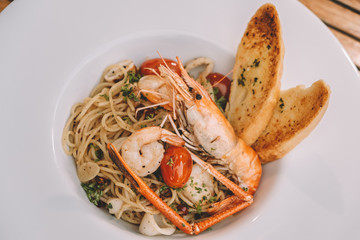 spaghetti pasta with shrimps and sweet basil on white plate over wooden table