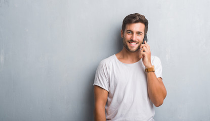 Handsome young man over grey grunge wall speaking on the phone with a happy face standing and smiling with a confident smile showing teeth