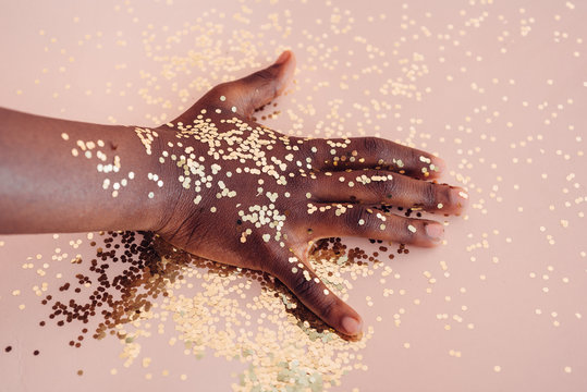 Black girl's hand with confetti on a pink background