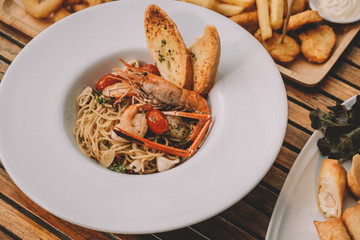 spaghetti pasta with shrimps and sweet basil on white plate over wooden table