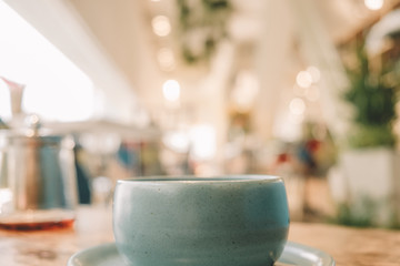 Ceramic Pastel Blue Tea cup on the wooden table with blur cafe background soft focus