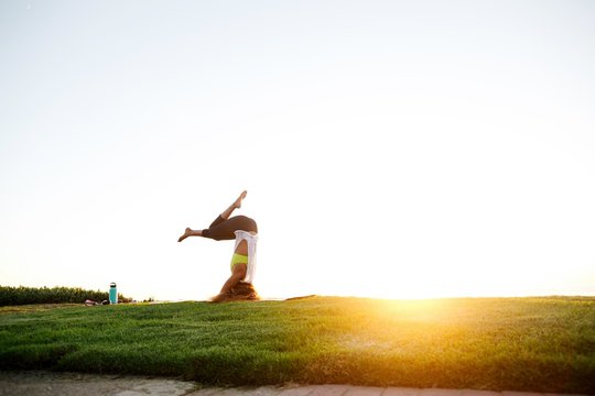 Fit, stylish woman practicing yoga at sunset on grass