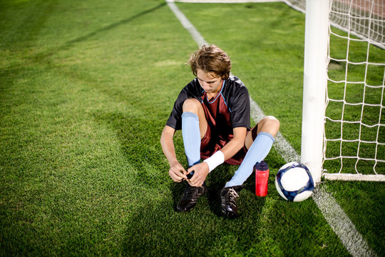 Young football player tying shoelaces in football stadium