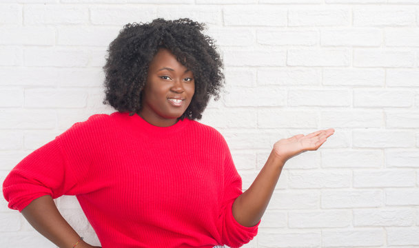 Young african american plus size woman over white brick wall smiling cheerful presenting and pointing with palm of hand looking at the camera. - Powered by Adobe