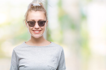 Young blonde woman wearing sunglasses over isolated background with a happy and cool smile on face. Lucky person.