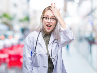 Young blonde doctor woman over isolated background surprised with hand on head for mistake, remember error. Forgot, bad memory concept.