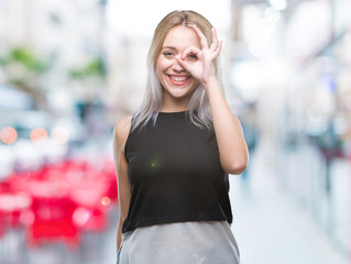 Young blonde woman over isolated background doing ok gesture with hand smiling, eye looking through fingers with happy face.