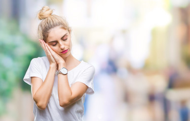 Young beautiful blonde woman wearing white t-shirt over isolated background sleeping tired dreaming and posing with hands together while smiling with closed eyes.