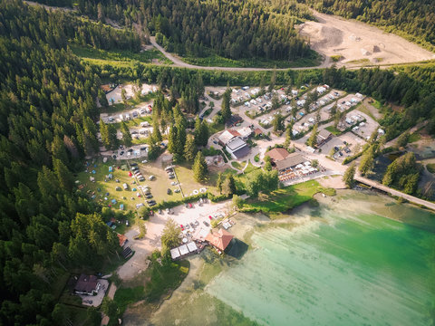 Aerial shot of the mountain lake surrounded by forest and green vast valley with a small camp site and local village