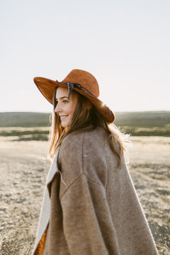 A portrait of a girl wearing beige poncho and a brown hat surrounded by icelandic majestic landscapes 
