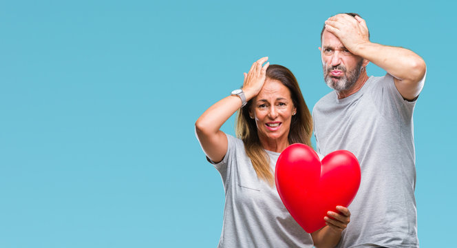 Middle age hispanic casual couple in love holding red heart over isolated background stressed with hand on head, shocked with shame and surprise face, angry and frustrated. Fear and upset for mistake.