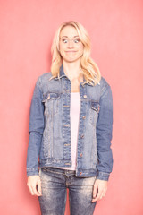 one young woman, 20-29 years old, long blond hair. Shot in studio on pink background. looking down, eyes wide open, face expression acting like a frog, standing still (upper body shot).