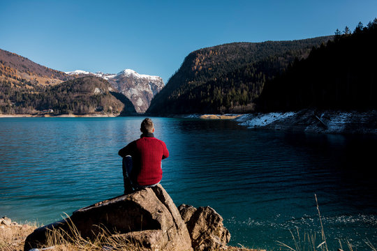Man walking down a cliff along a lake on mountains