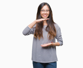 Young asian woman wearing glasses over isolated background gesturing with hands showing big and large size sign, measure symbol. Smiling looking at the camera. Measuring concept.