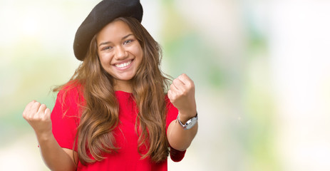 Young beautiful brunette fashion woman wearing red t-shirt and black beret over isolated background very happy and excited doing winner gesture with arms raised, smiling and screaming for success