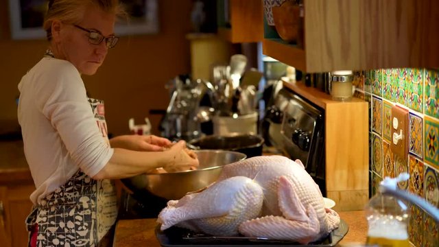Mature woman preparing a turkey for Thanksgiving putting stuffing into the cavity.