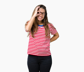 Obraz na płótnie Canvas Young beautiful brunette woman wearing glasses and stripes t-shirt over isolated background doing ok gesture with hand smiling, eye looking through fingers with happy face.