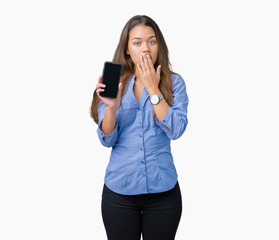 Young beautiful brunette business woman showing screen of smartphone over isolated background cover mouth with hand shocked with shame for mistake, expression of fear, scared in silence