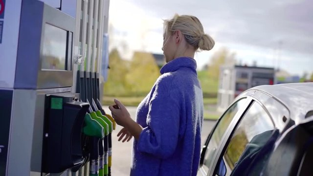 female driver is holding a hose at gas station, fueling gasoline in car independently