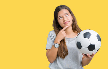 Young beautiful brunette woman holding soccer football ball over isolated background serious face thinking about question, very confused idea