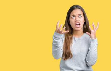 Young beautiful brunette woman wearing sweater over isolated background crazy and mad shouting and yelling with aggressive expression and arms raised. Frustration concept.