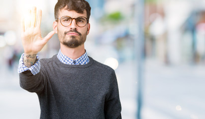 Young handsome smart man wearing glasses over isolated background doing stop sing with palm of the hand. Warning expression with negative and serious gesture on the face.