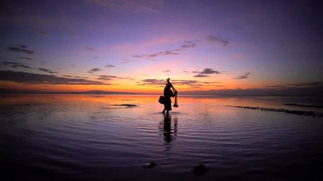 Balinese male in silhouette fishing with a net on a sunset beach in Indonesia